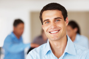 Closeup portrait of happy business man smiling with colleagues in background